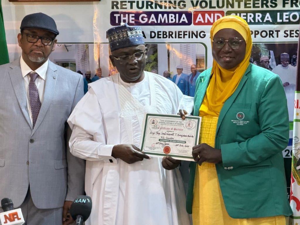 DG NTAC, Rt. Hon. Yusuf Buba Yakub, presenting a Certificate of Service to a Returning Volunteer, Prof. Nazmat Surajudeen Bakinde, Vice-Chancellor of the Gambia University of Applied Science, Engineering and Technology (USET), while the Director of Programmes, Amb. Bello A. Jaye, looks on at the Debriefing and Support Session on *1st July, 2026.*